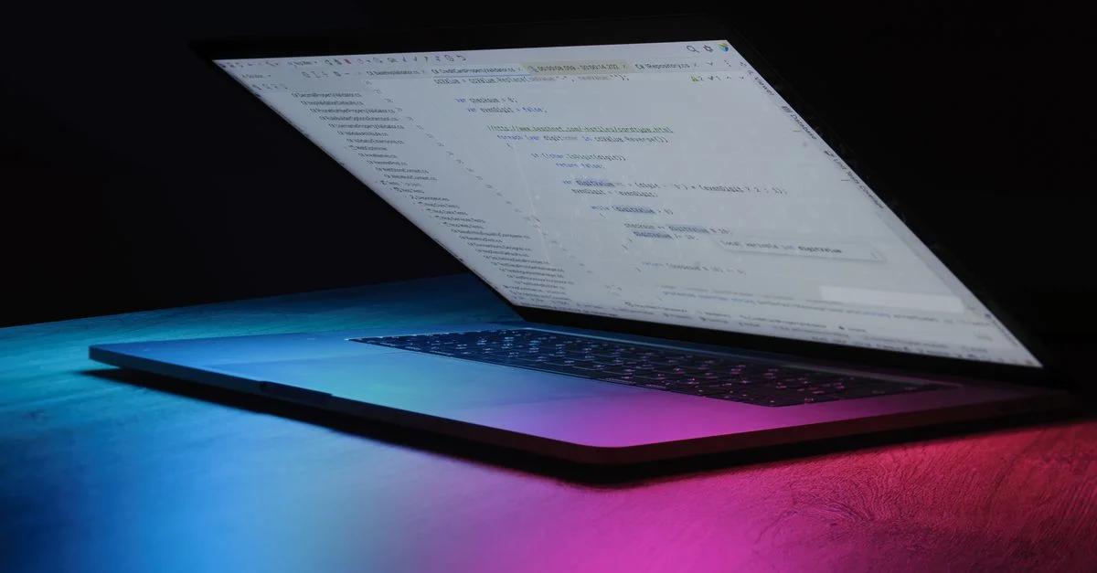 Un ordinateur portable partiellement ouvert affichant du code, baigné dans un éclairage néon vibrant.