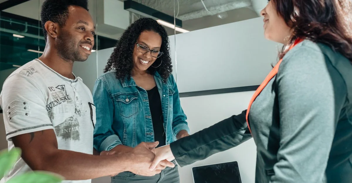 Couple souriant se serrant la main avec un conseiller dans un bureau moderne.